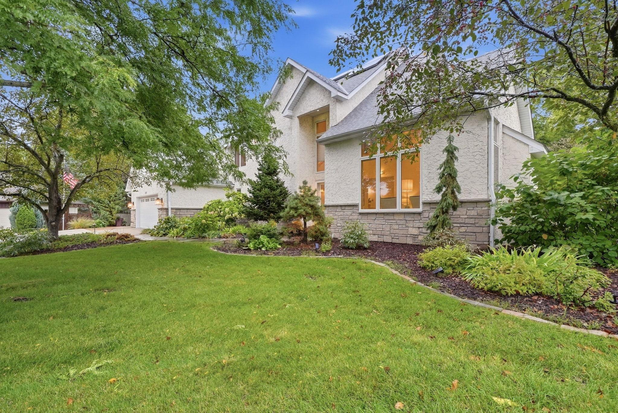 Two-story stucco home with a stone facade, attached garage, and landscaped front lawn.