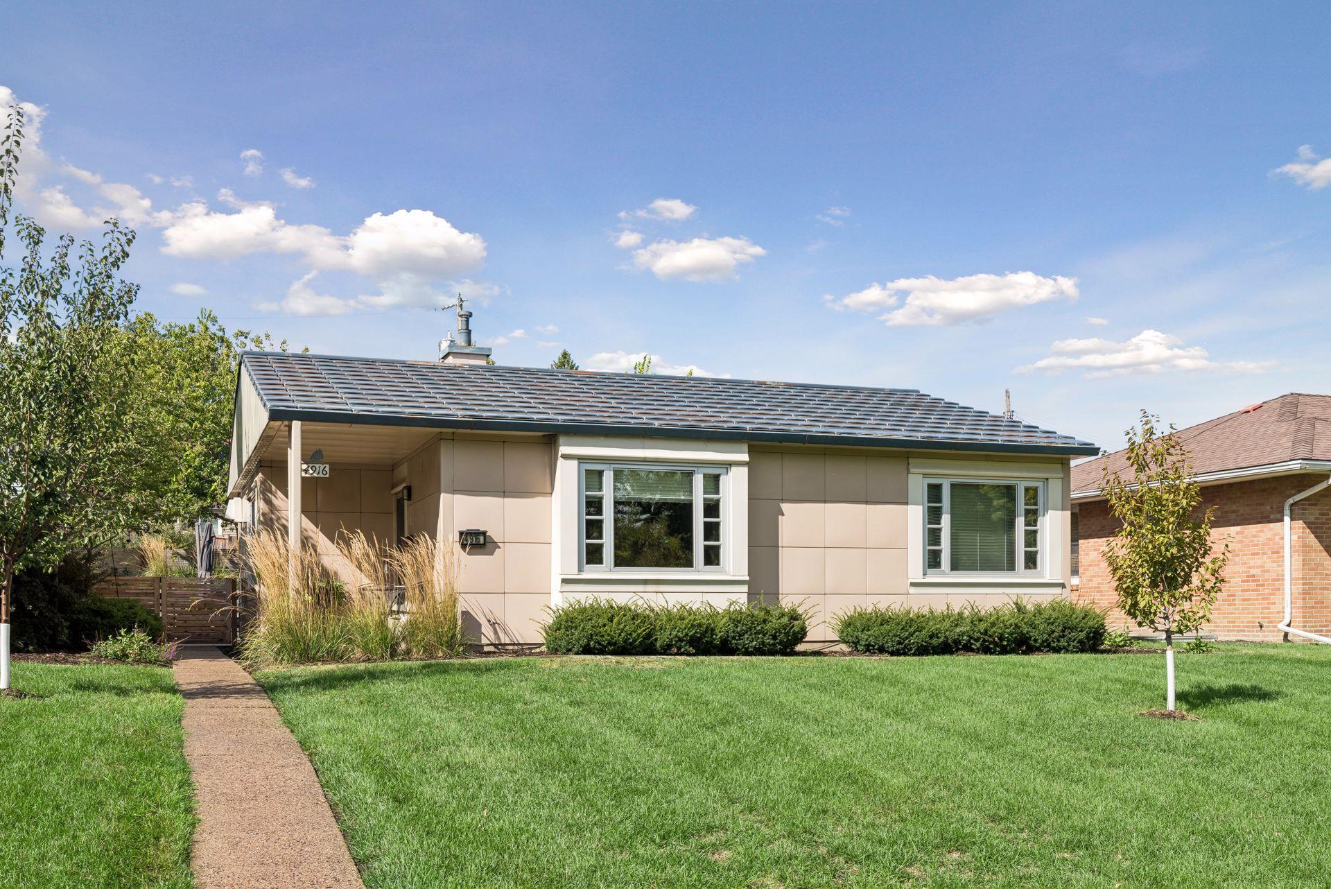 Single-story tan home with a dark tiled roof, white-trimmed windows, and a front lawn.