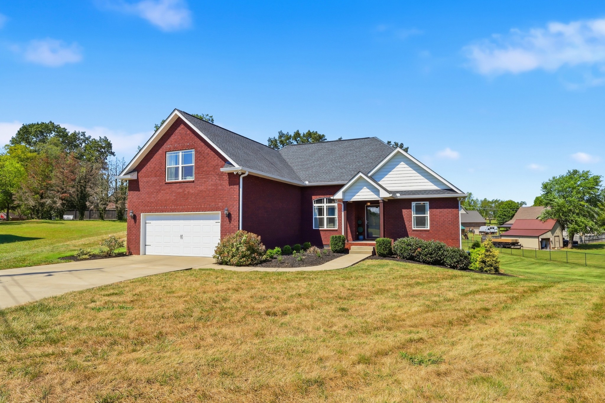 Red brick house with an attached garage, curved front walkway, and broad grassy lawn.