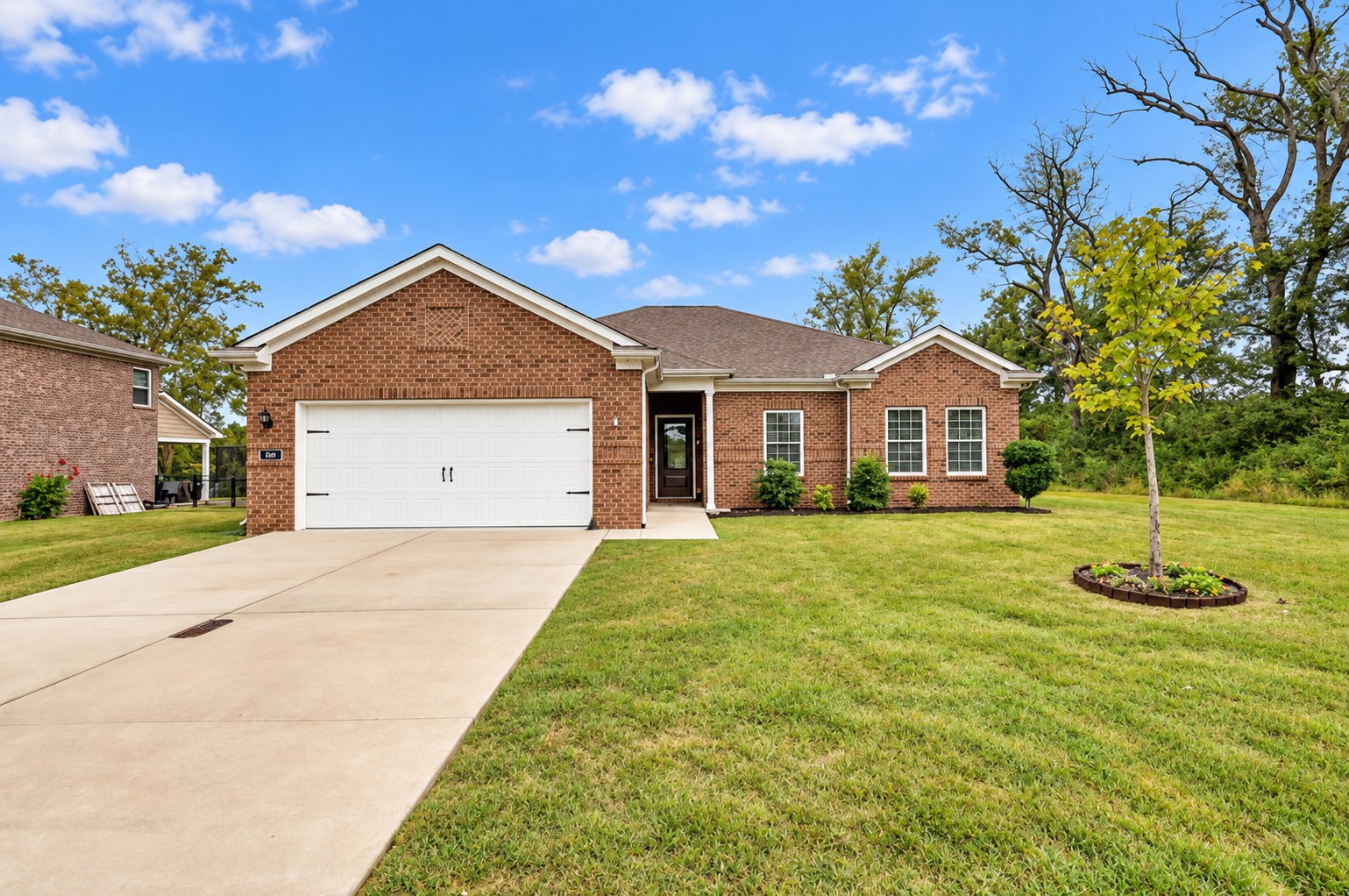 Red-brick home with a white double garage, wide driveway, and large green lawn.