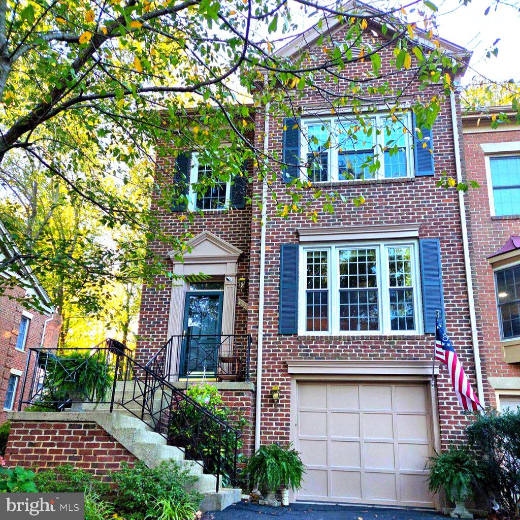 Brick townhouse with blue shutters, front steps, attached garage, and an American flag.