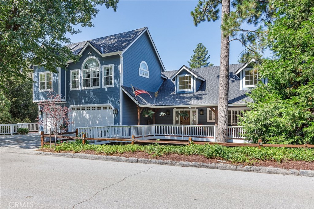Blue two-story home with white railings, an attached garage, and mature trees.