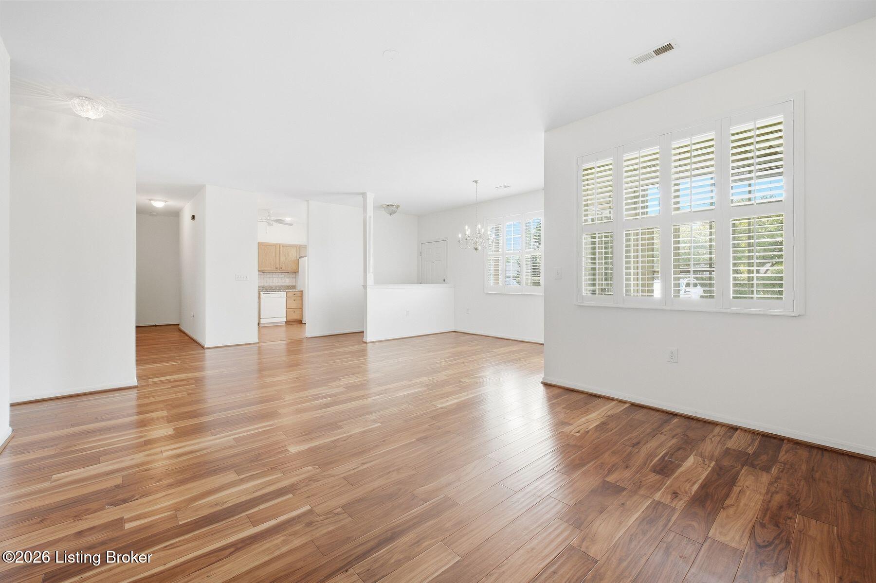Vacant open-plan living and dining area with hardwood floors, plantation shutters, and a glimpse of the kitchen.