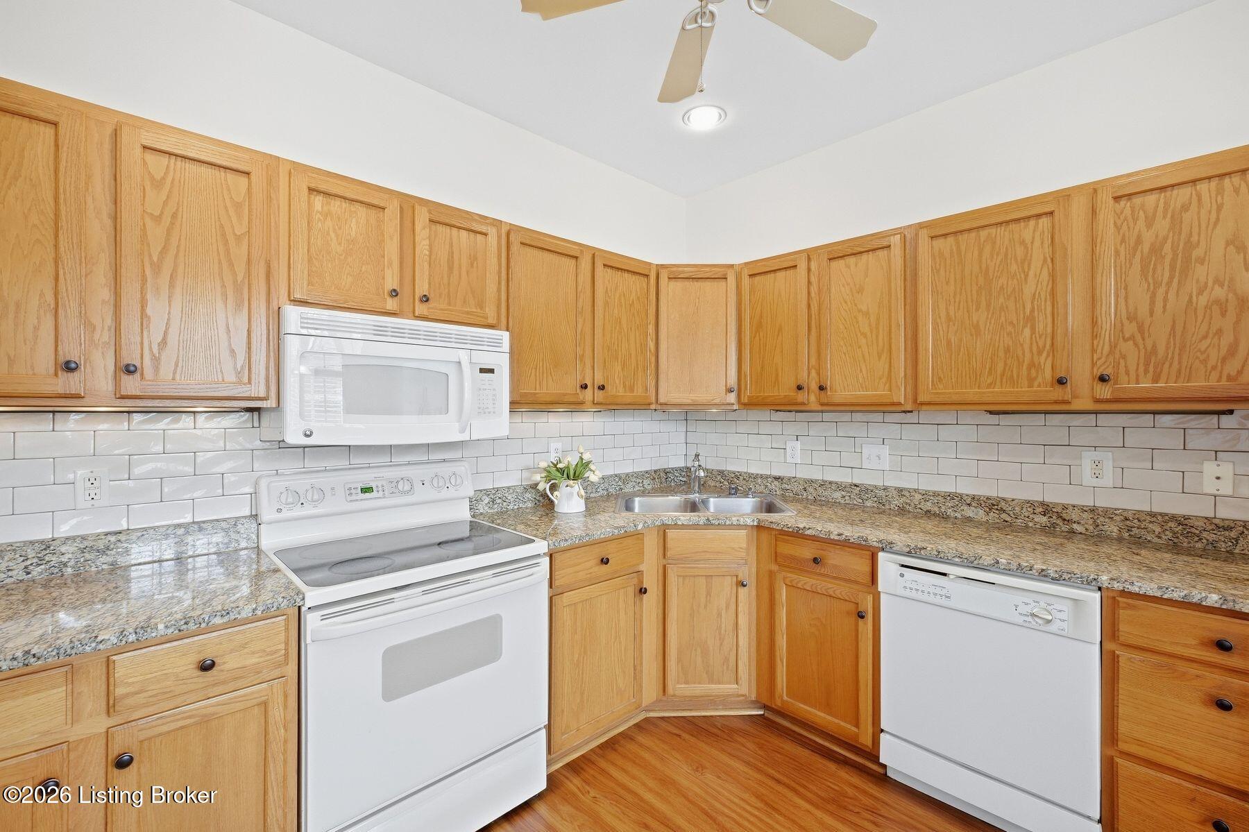 Kitchen with honey-oak cabinets, granite counters, white appliances, and a subway-tile backsplash.