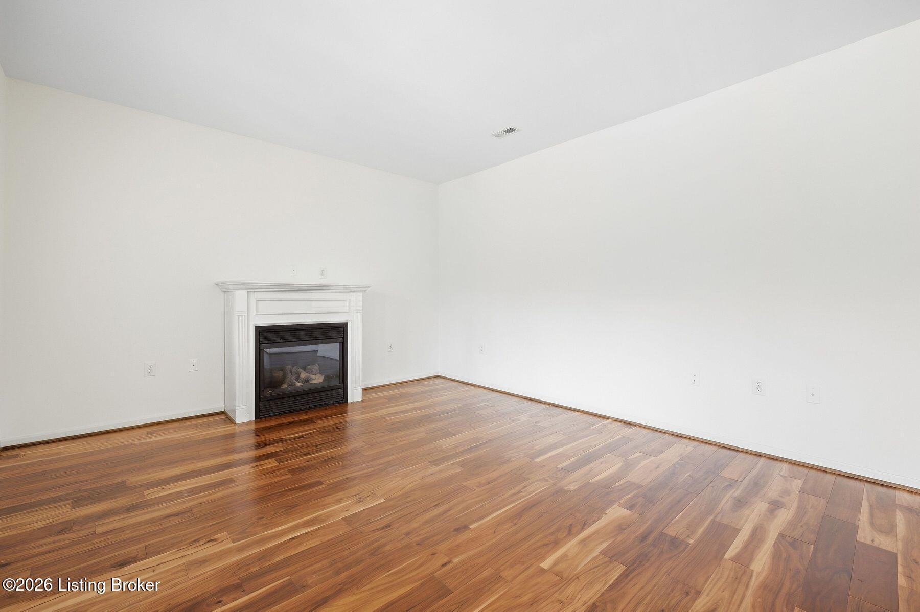 Empty living room with hardwood floors and a white-trimmed gas fireplace.