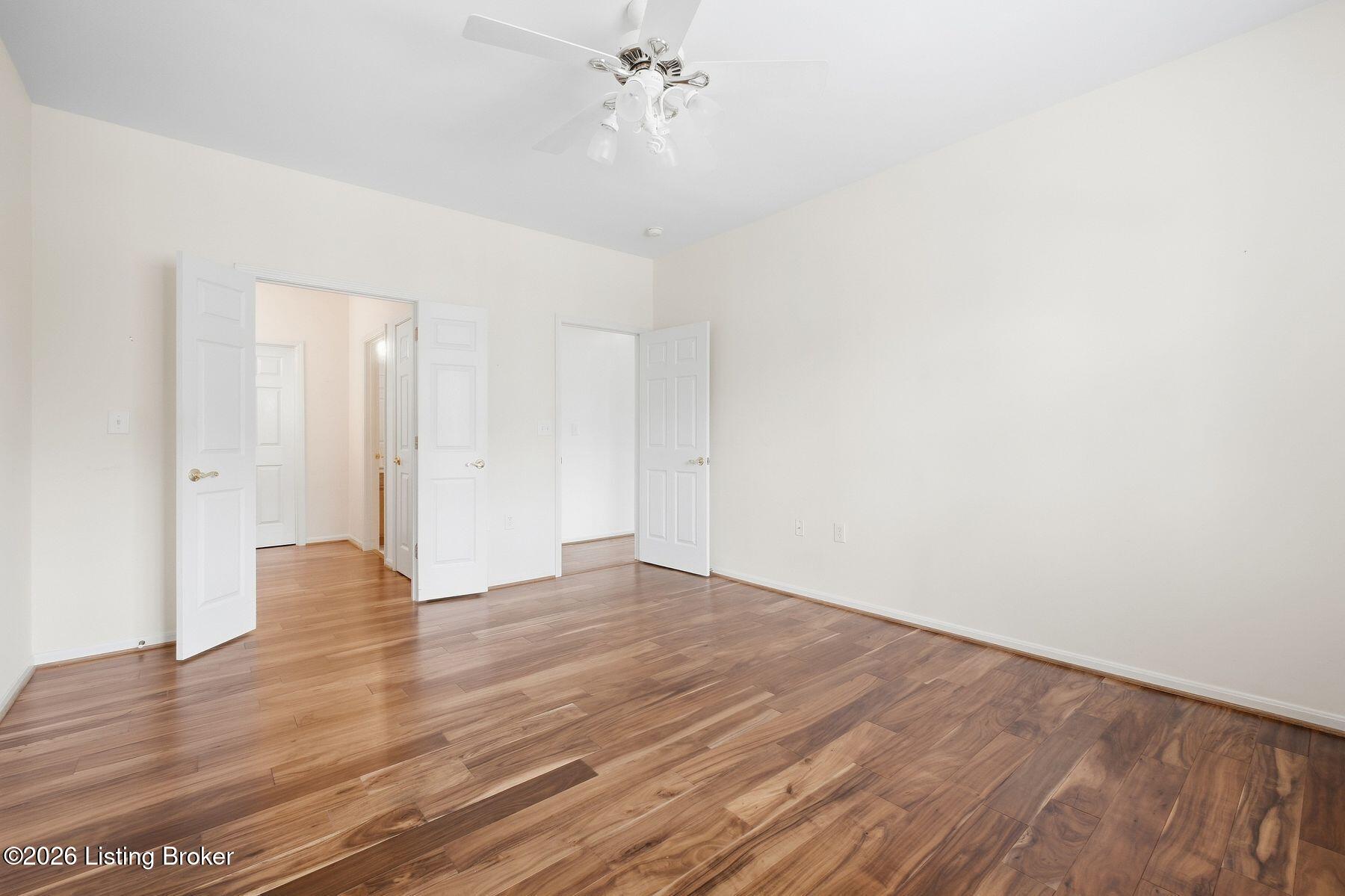 Empty room with wide-plank wood flooring, a ceiling fan, and several open doors.
