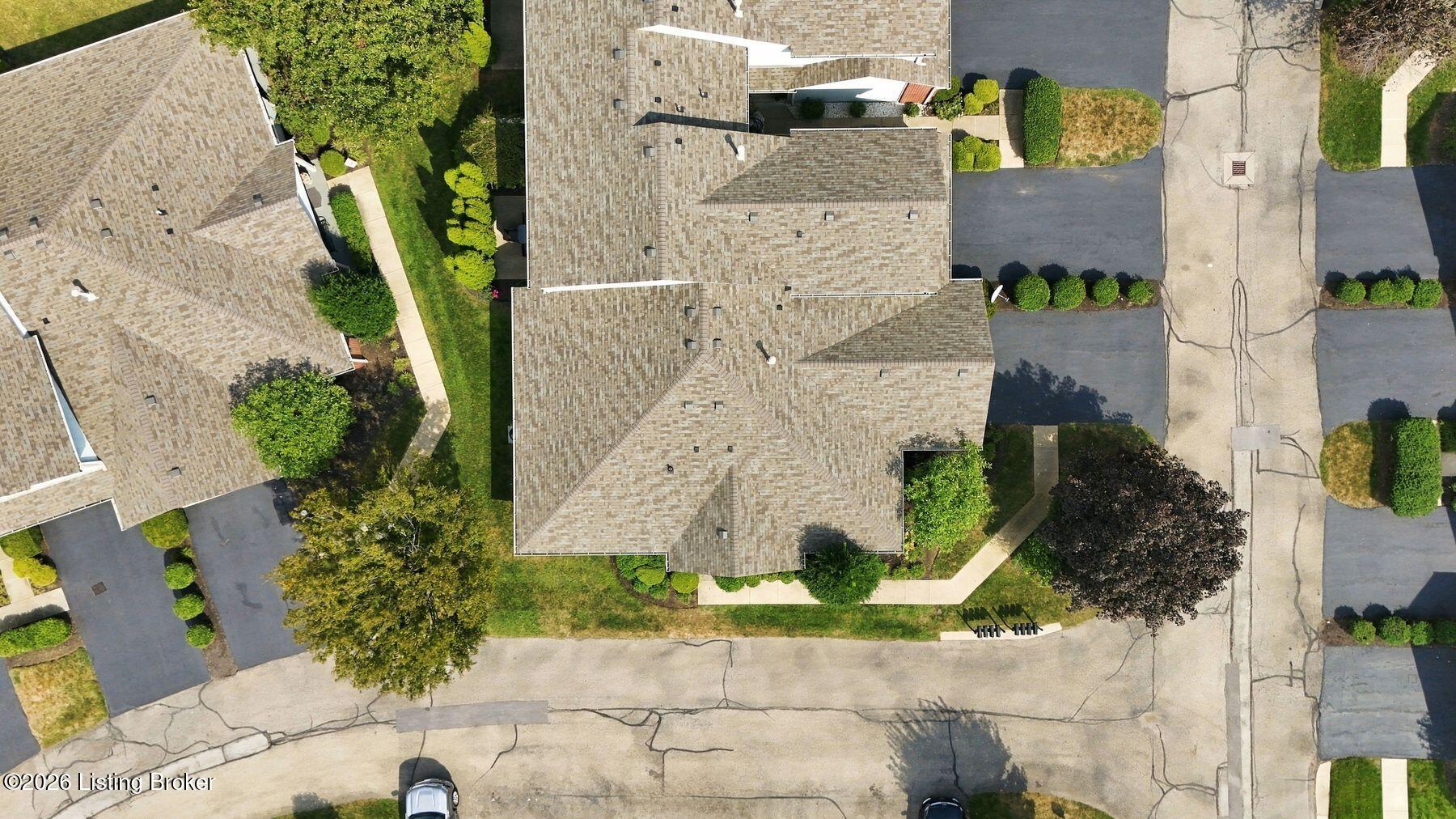 Aerial view of a residential building with a broad shingle roof, parking areas, sidewalks, and landscaping.