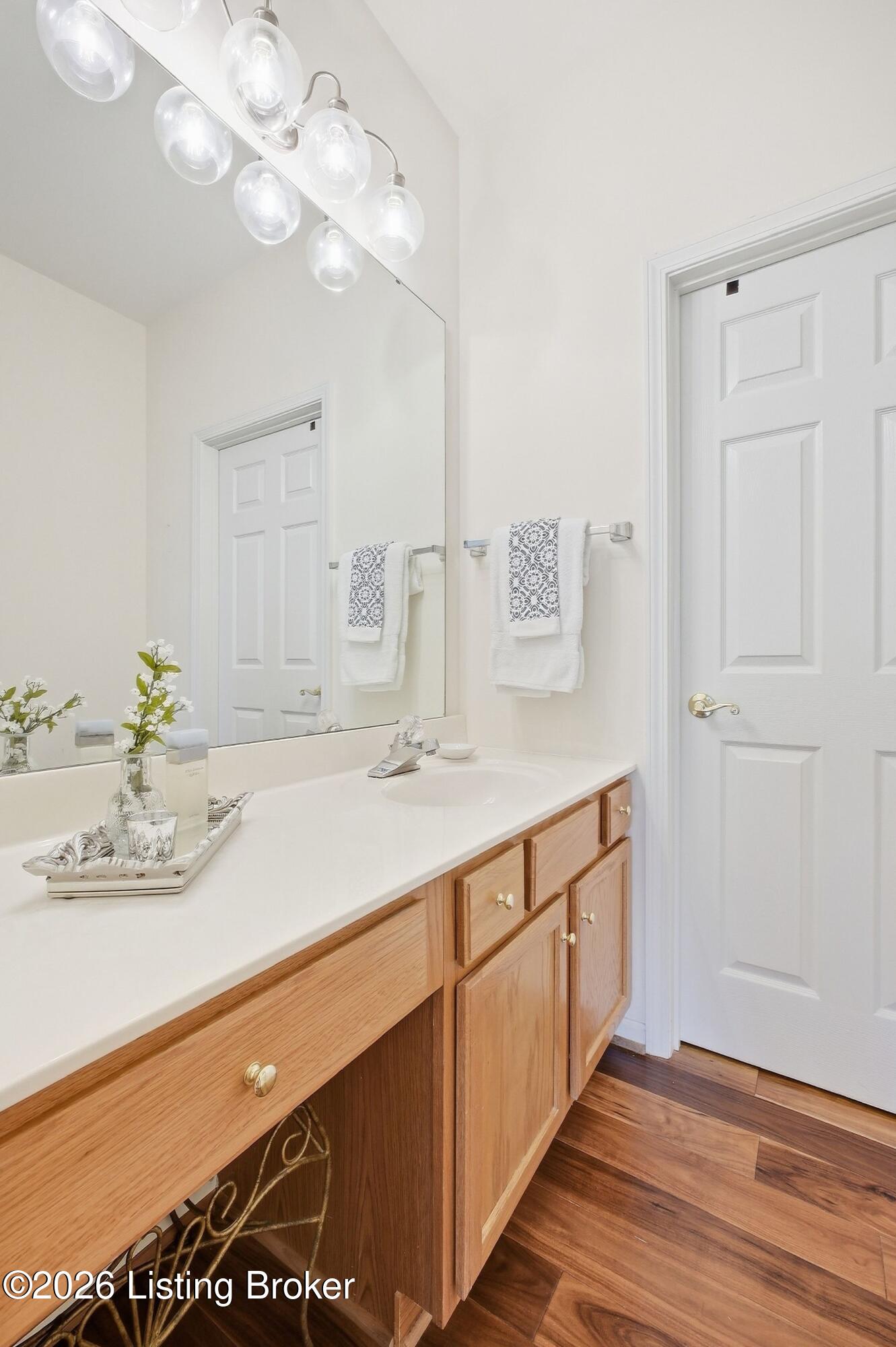 Bathroom vanity with light wood cabinets, a large mirror, and dark wood flooring.