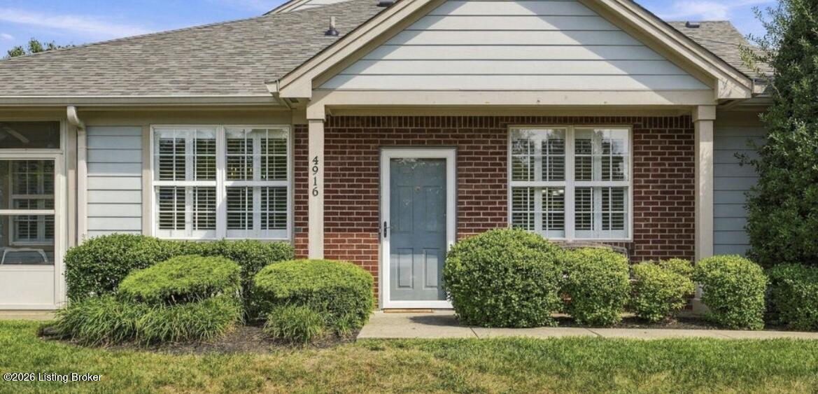 Home exterior with a red brick facade, blue front door, covered entry, and trimmed shrubs.