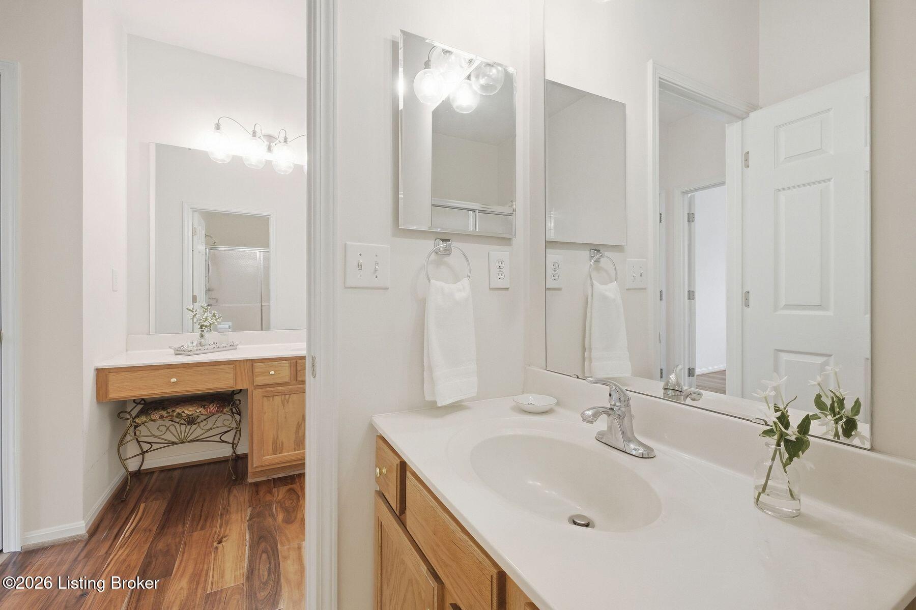 Bathroom vanity with a wide mirror, light wood cabinetry, and a vase of flowers.