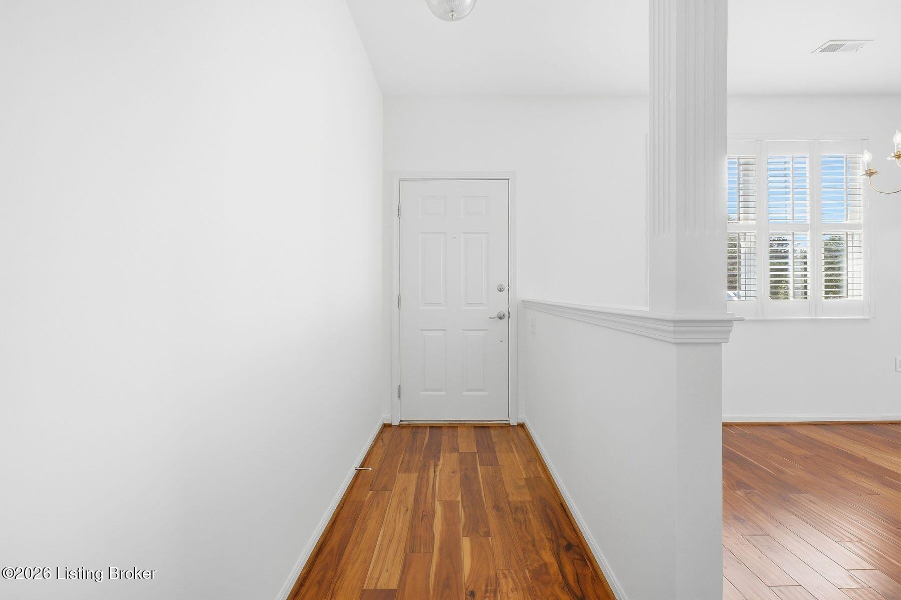 Entry foyer with hardwood floors, white front door, and plantation-shuttered windows.