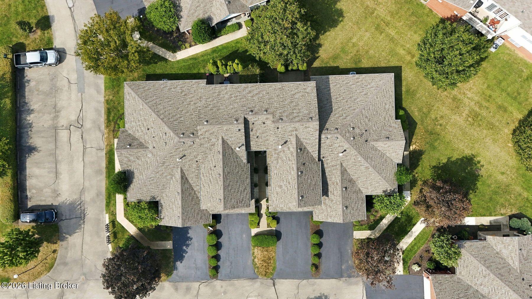 Aerial view of a residential building with a large shingle roof and surrounding parking and lawns.
