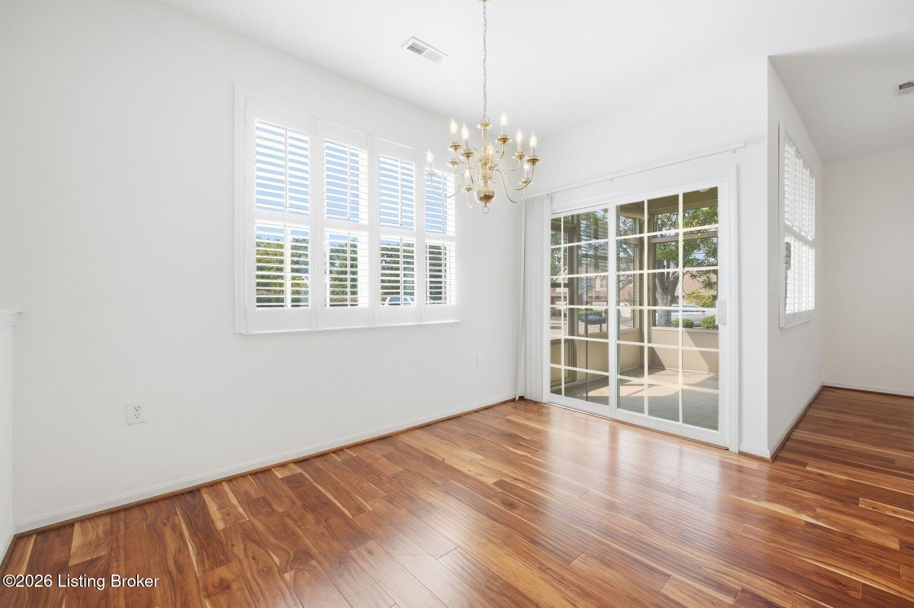 Empty dining room with polished wood floors, plantation shutters, and a sliding glass door to the patio.