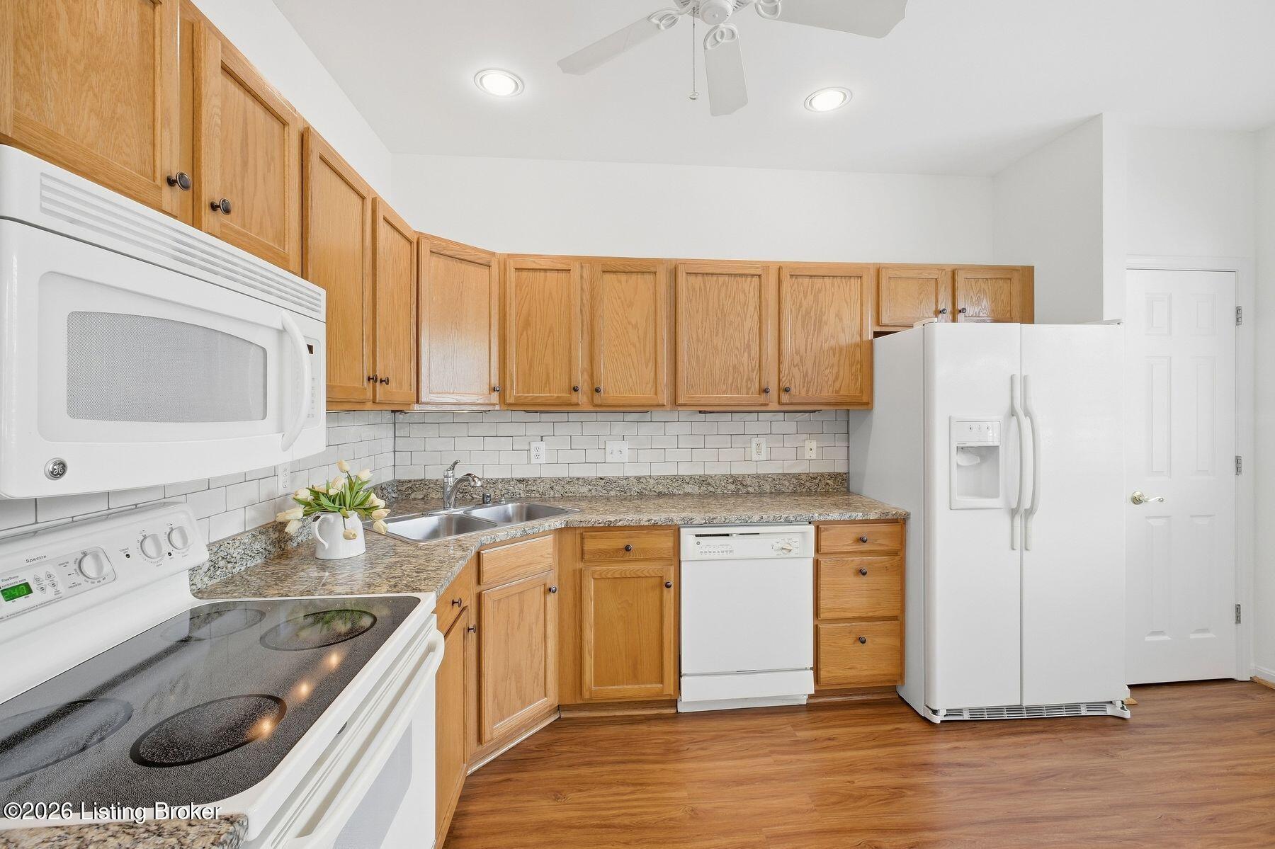 Kitchen with oak cabinets, granite counters, white appliances, and a subway-tile backsplash.
