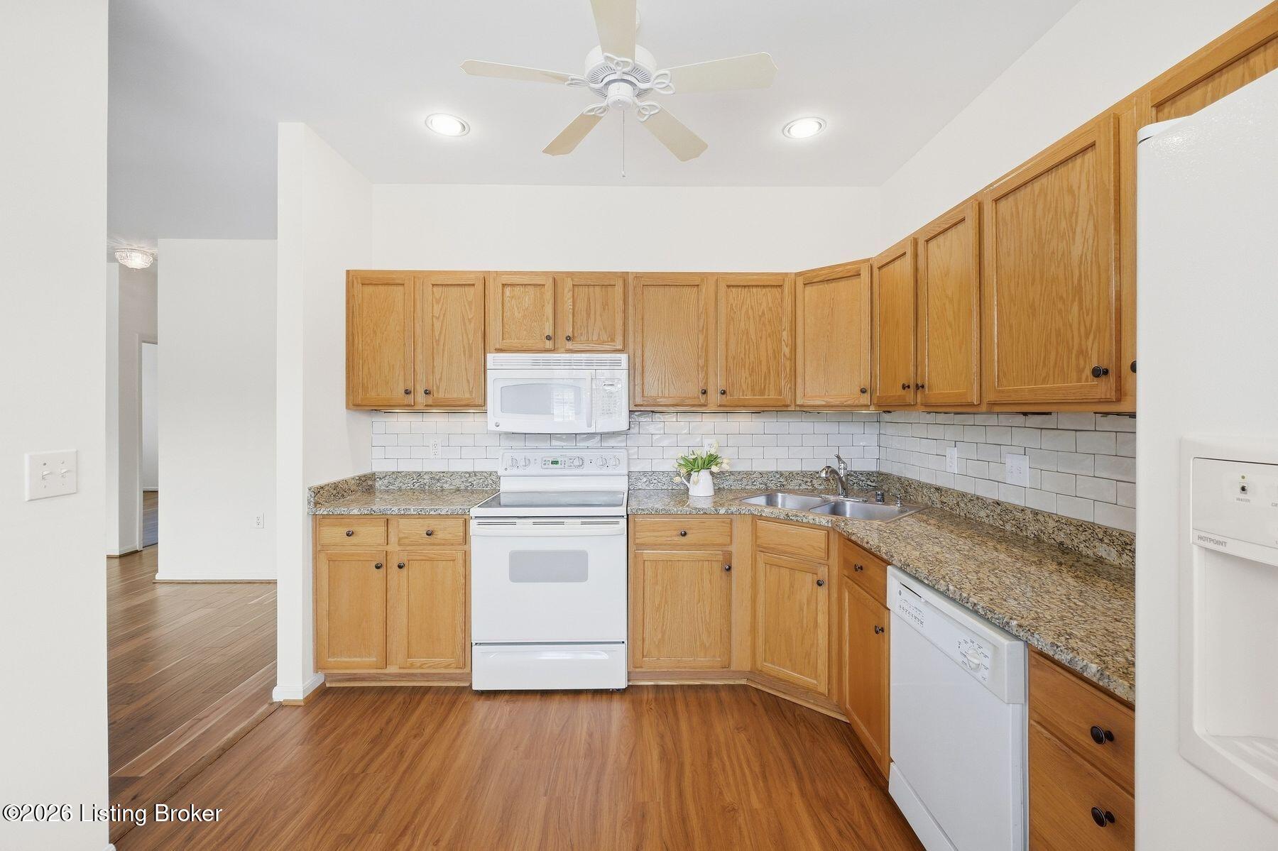 Kitchen with honey-oak cabinets, granite counters, white subway-tile backsplash, and white appliances.