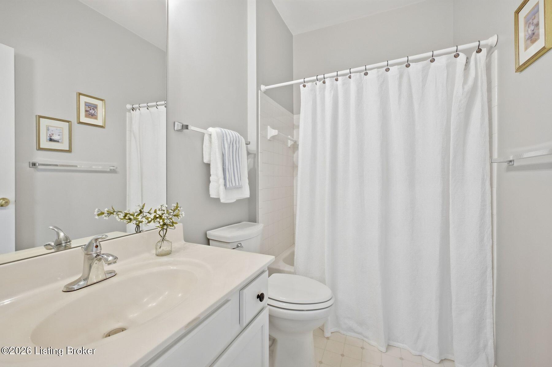 Bathroom with white vanity, toilet, and tub behind a shower curtain.