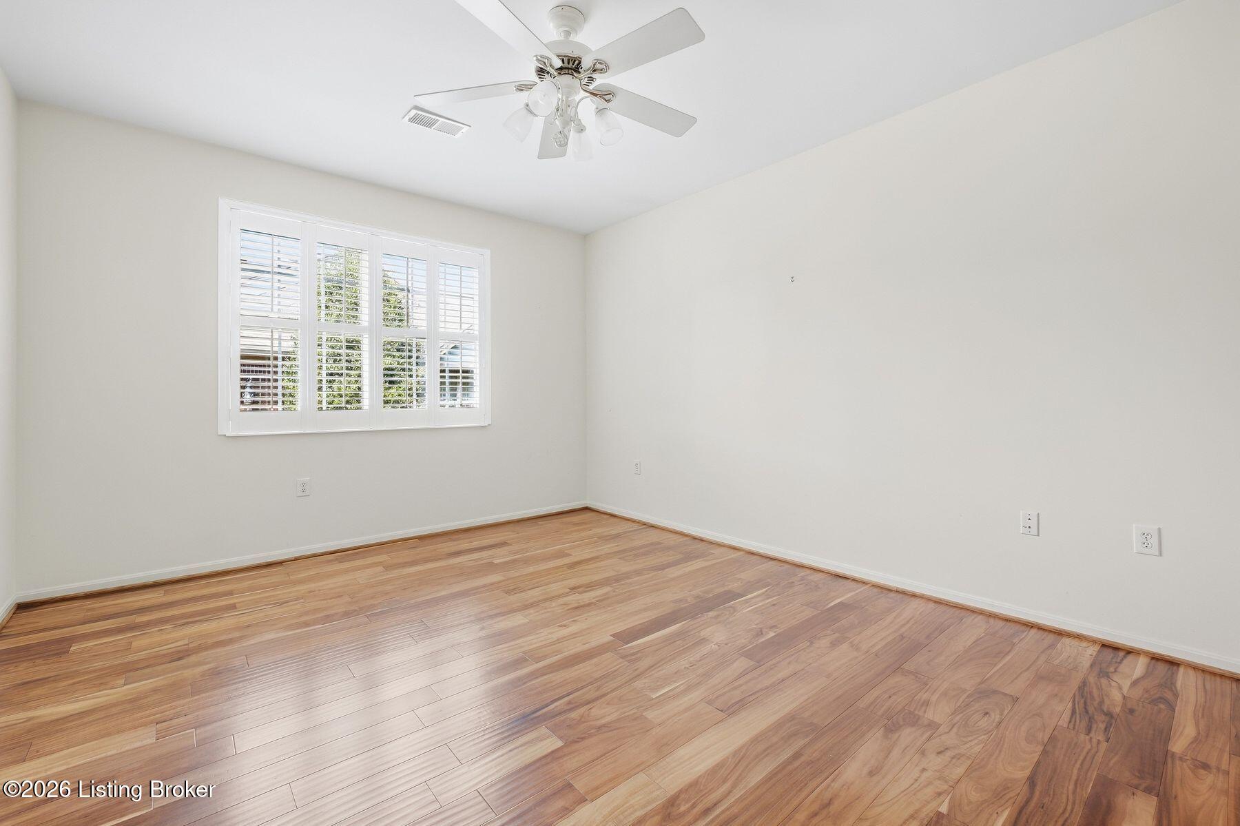 Vacant room with hardwood floors, plantation shutters, and a ceiling fan.