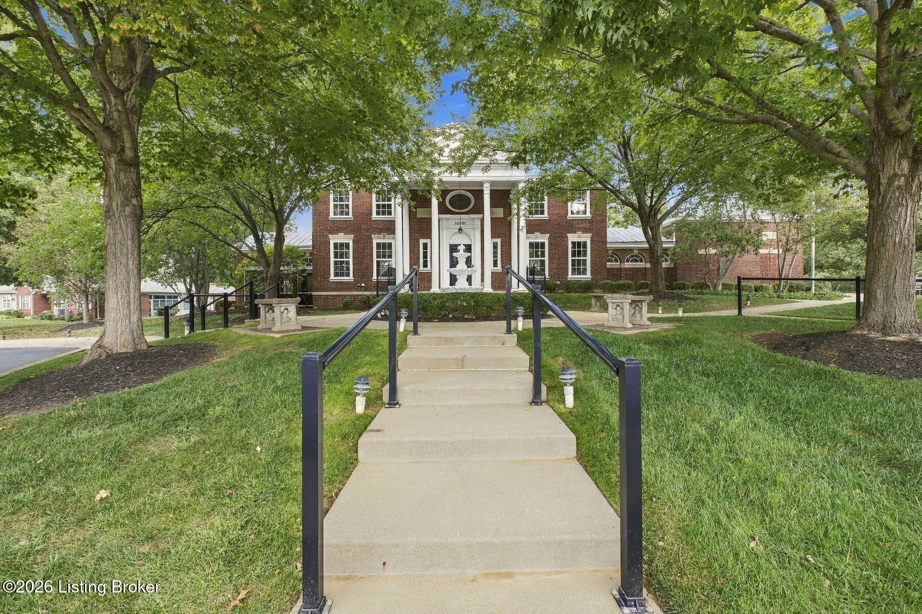 Brick building entrance framed by mature trees, with a central fountain and broad front steps.