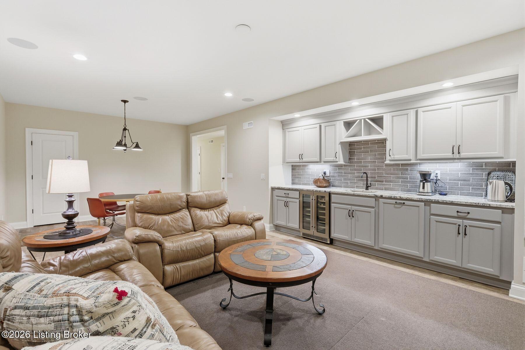 Living room with tan leather seating and a built-in kitchenette with white cabinetry and gray tile backsplash.