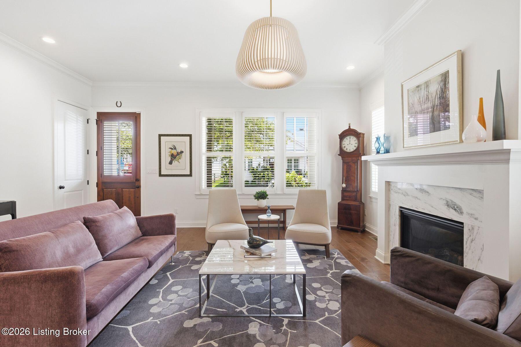 Living room with a marble-surround fireplace, mauve sofas, cream chairs, and shuttered windows.