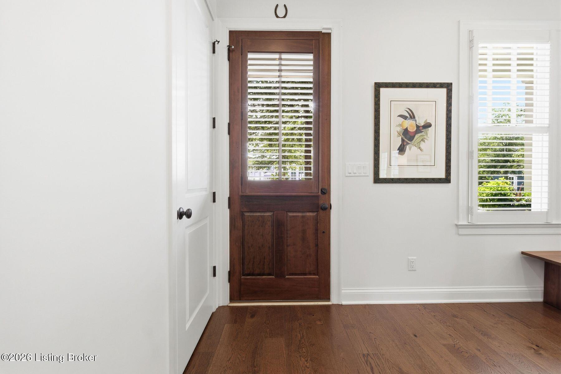 Entry hall with a dark wood front door, hardwood floors, and shuttered window.