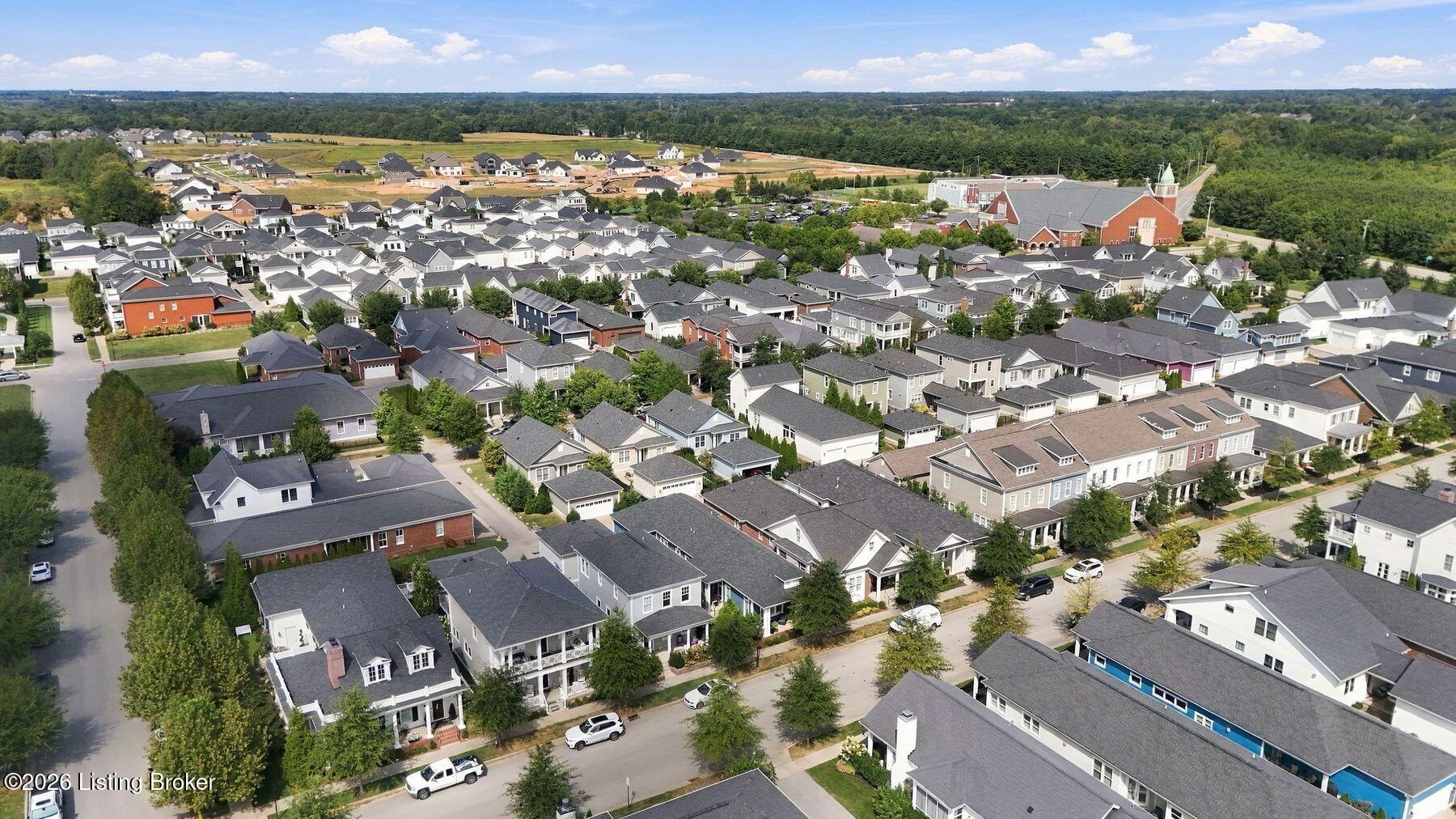 Aerial view of a residential neighborhood with tree-lined streets, a red-brick church, and woods beyond.