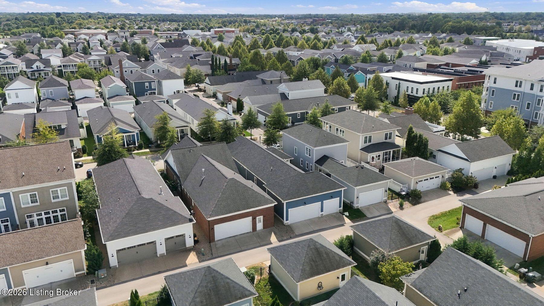 Aerial view of a residential neighborhood with detached homes, tree-lined streets, and nearby commercial buildings.