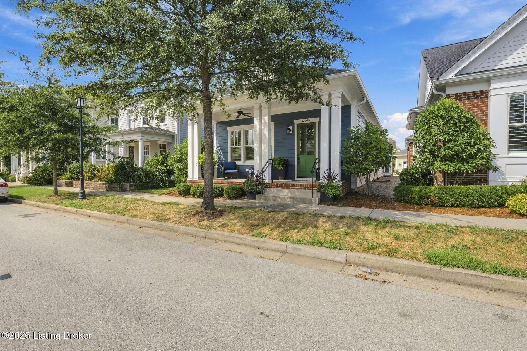 Blue-sided home with a green front door, white-columned porch, and mature tree in the front yard.