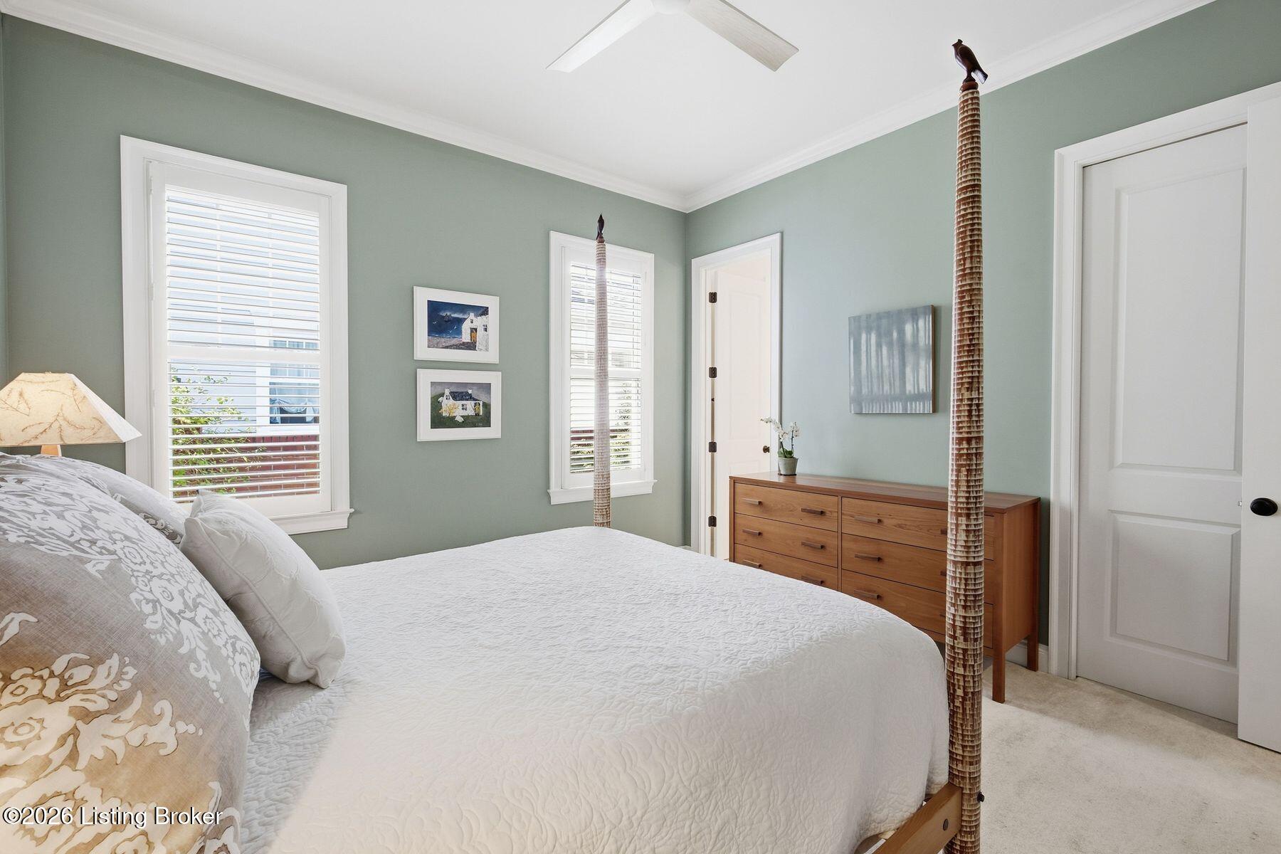 Bedroom with a white quilted bed, sage-green walls, shuttered windows, and a wooden dresser.