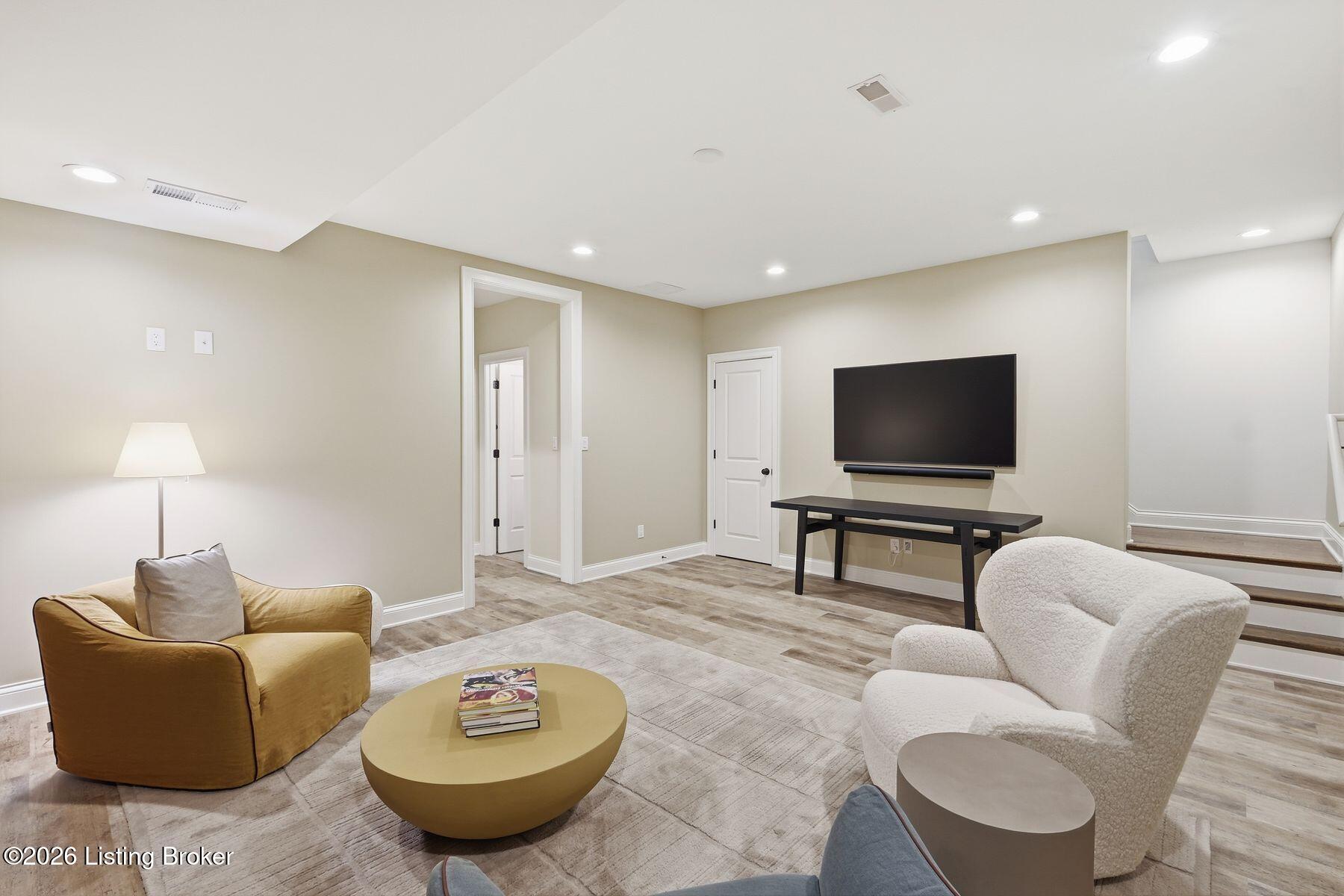 Furnished living room with a wall-mounted TV, mustard-yellow armchair, and stairs.