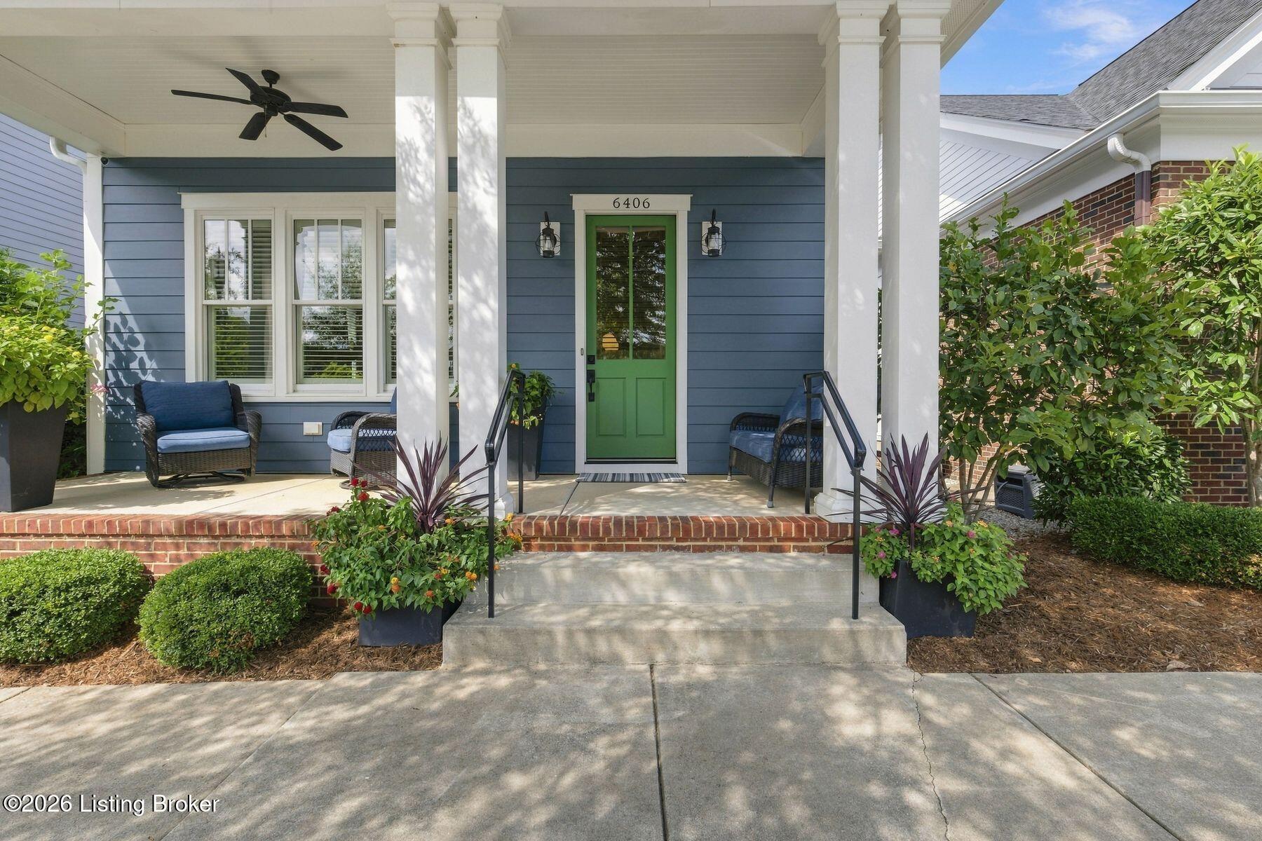 Blue home’s covered front porch with white columns, wicker seating, and a green door.