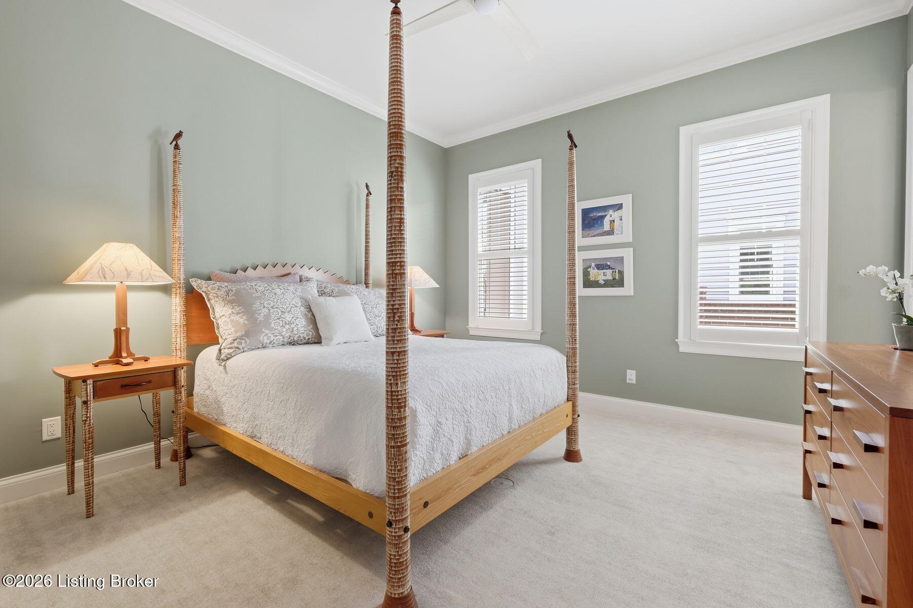 Bedroom with a tall wooden four-poster bed, white bedding, sage-green walls, and two bright windows.