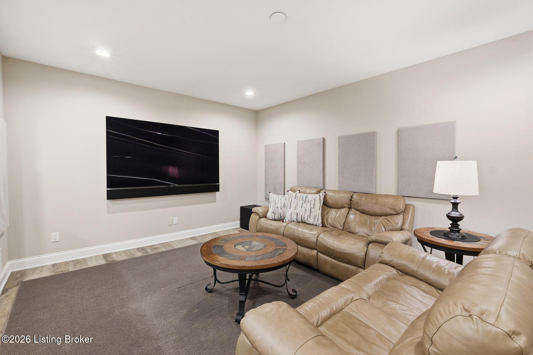 Furnished media room with tan leather sectional sofas and a large wall-mounted television.