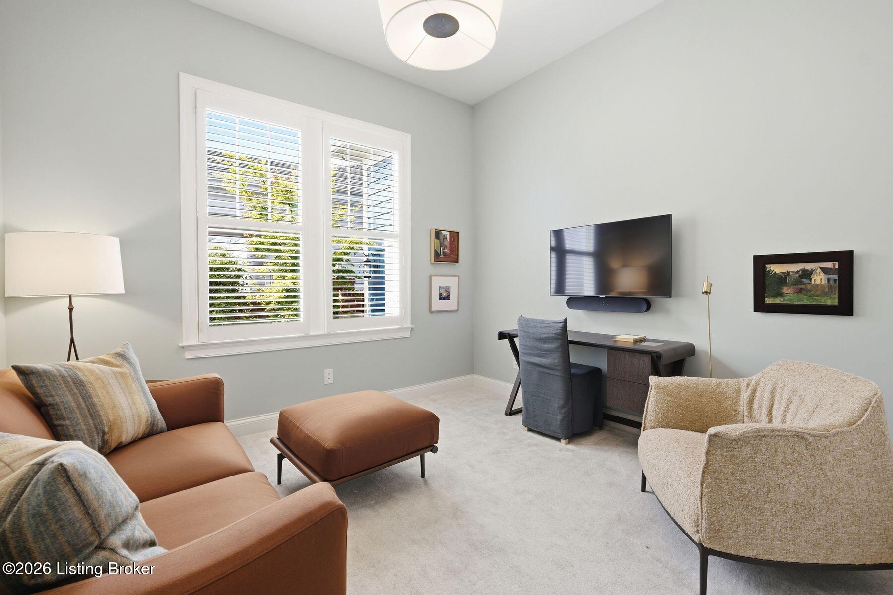Furnished sitting room with plantation-shuttered windows, a leather sofa, cream armchair, and wall-mounted television.