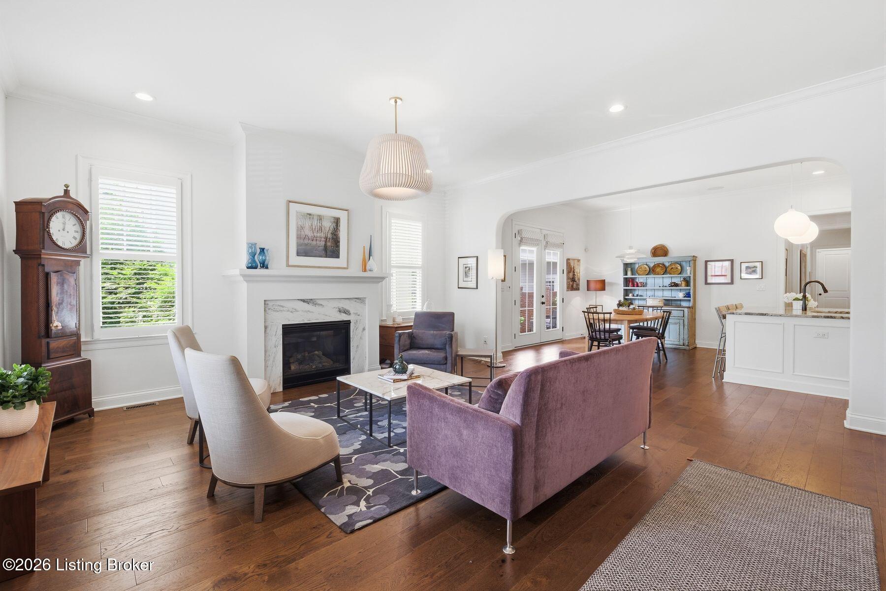 Living room with a marble fireplace, purple sofa, hardwood floors, and an open dining and kitchen area.