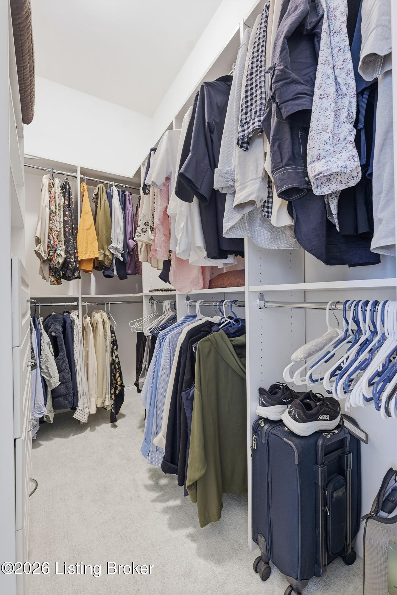 Walk-in closet with built-in shelving, hanging clothes, shoes, and rolling suitcases.