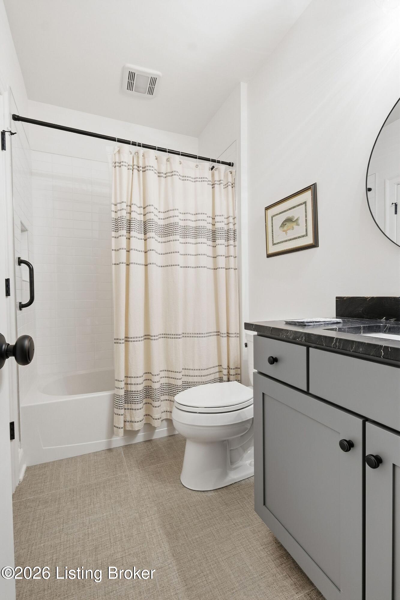 Bathroom with striped shower curtain, white tub and toilet, and gray vanity with black marble countertop.