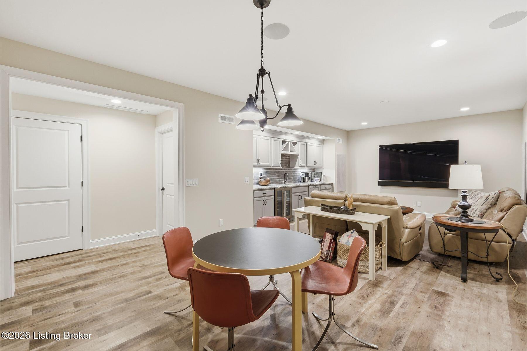 Open-plan living and dining area with a round table, beige leather seating, and a compact kitchen.