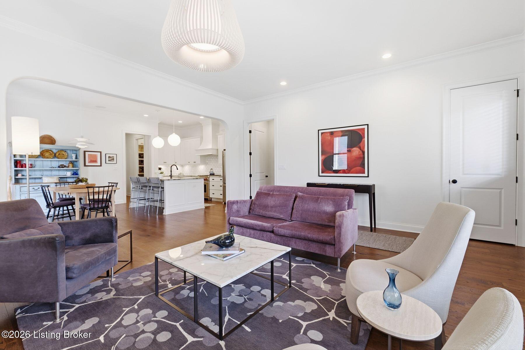 Furnished living room with purple sofas and an open view into the dining area and kitchen.