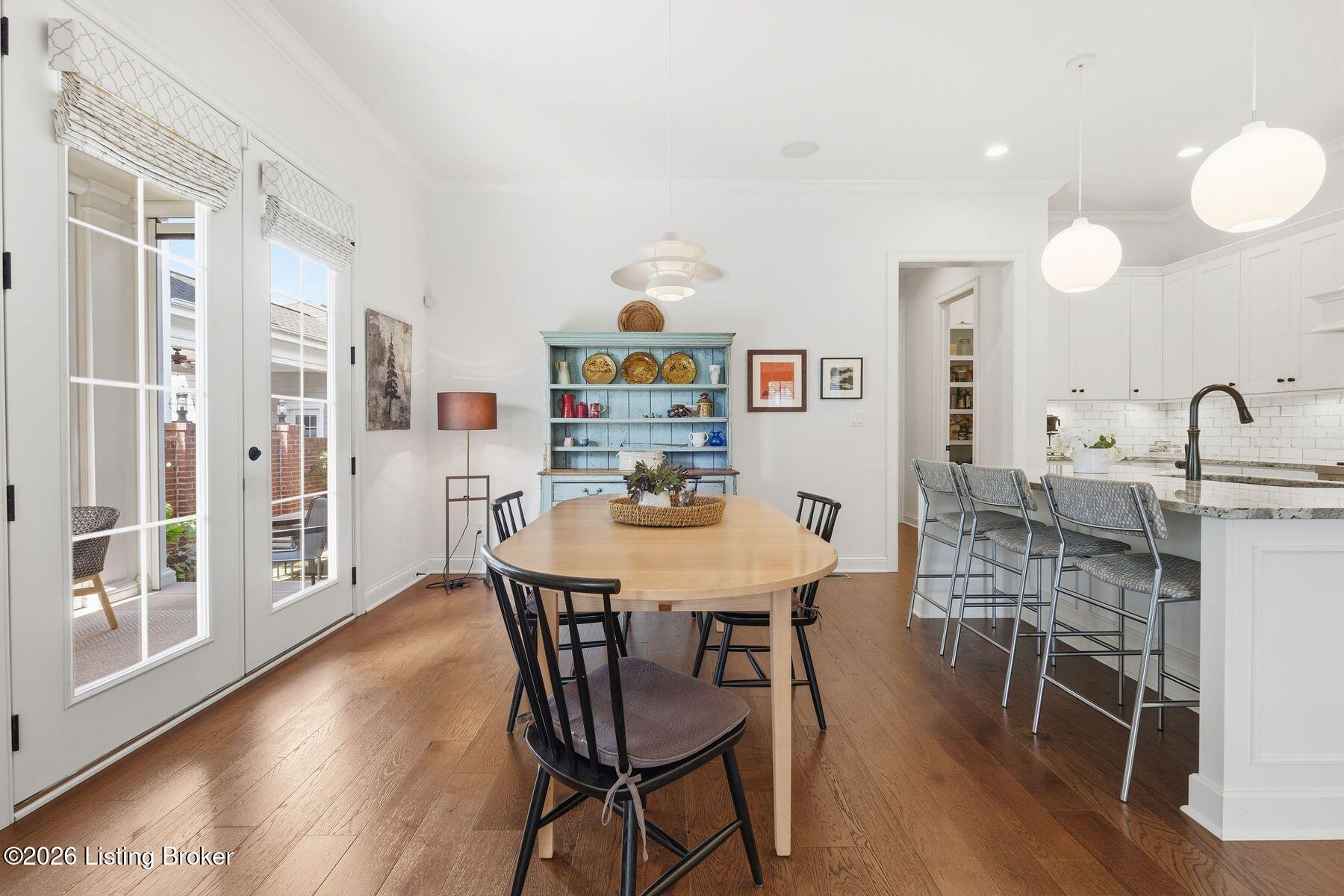 Dining room with a wooden table, blue hutch, hardwood floors, and an adjoining white kitchen.
