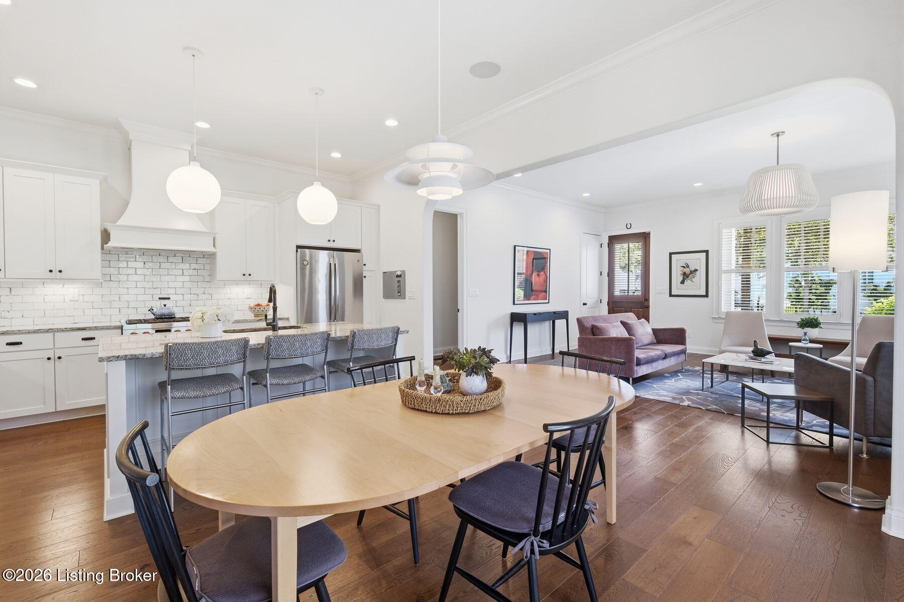 Open-plan kitchen and living room with a marble island, wood dining table, and hardwood floors.