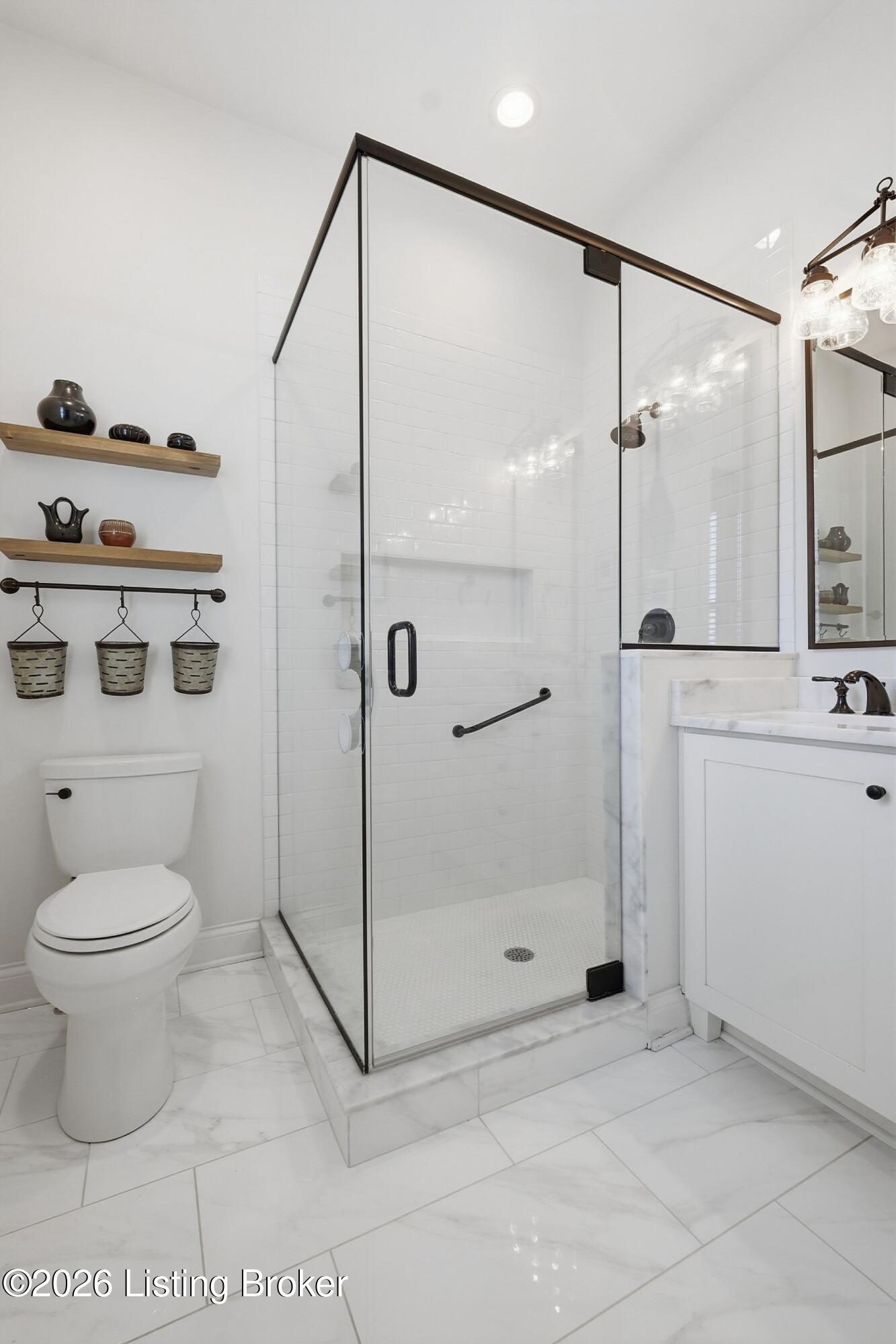 Bathroom with a glass-enclosed walk-in shower, marble tile, white vanity, and wooden display shelves.