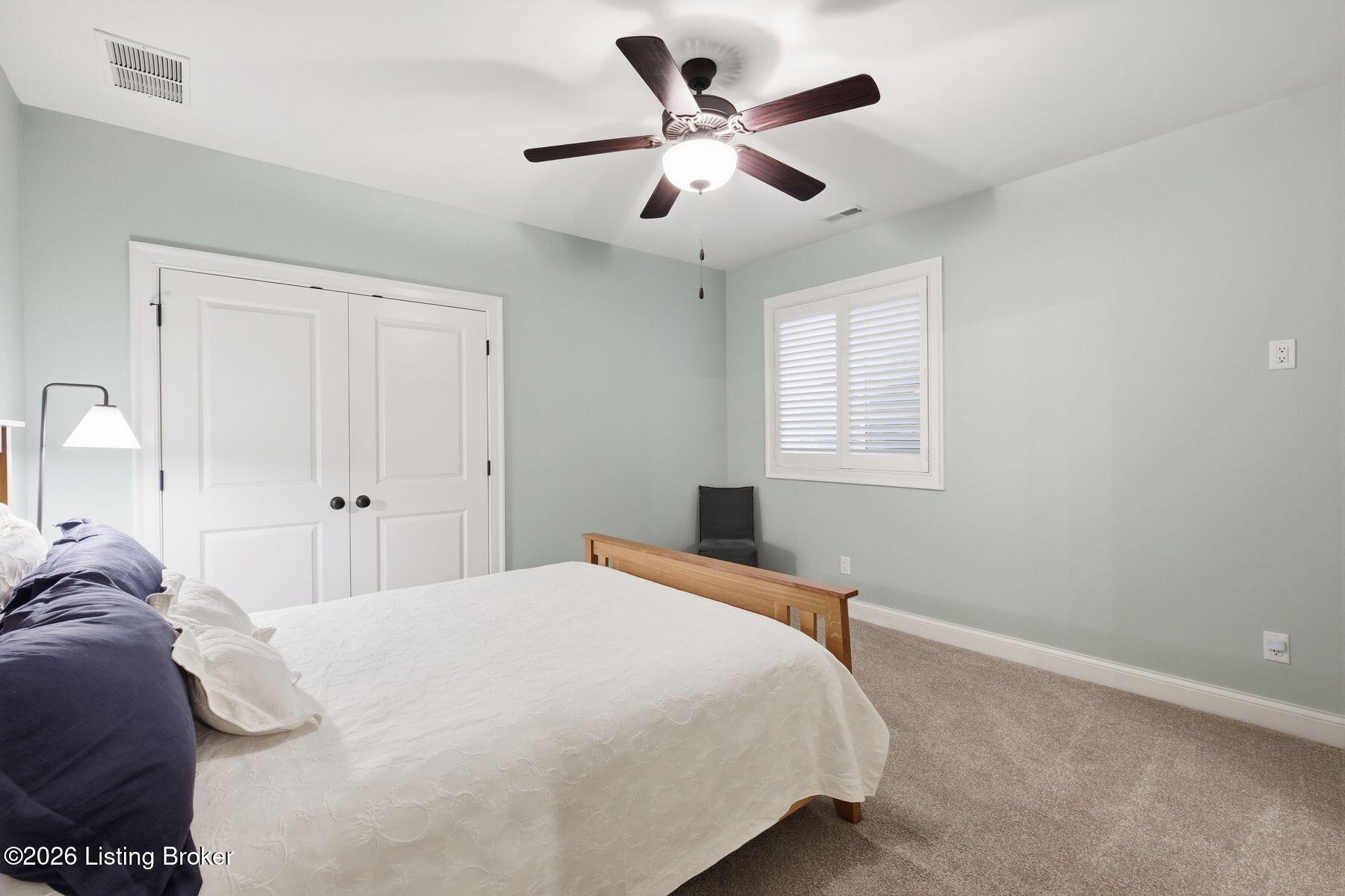 Bedroom with white bed, dark blue pillows, pale green walls, and ceiling fan.