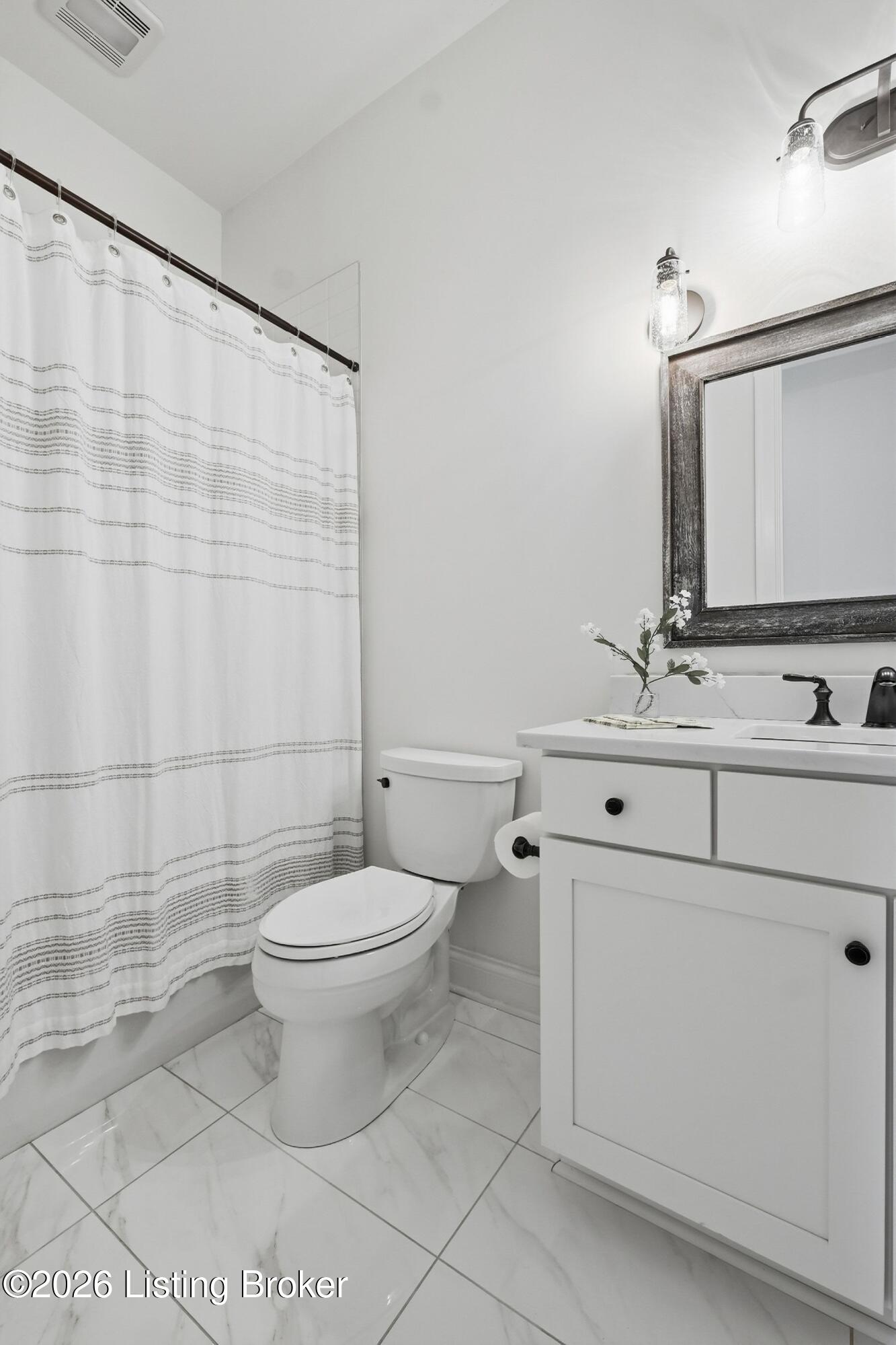 Bathroom with a white vanity, framed mirror, toilet, and striped shower curtain.