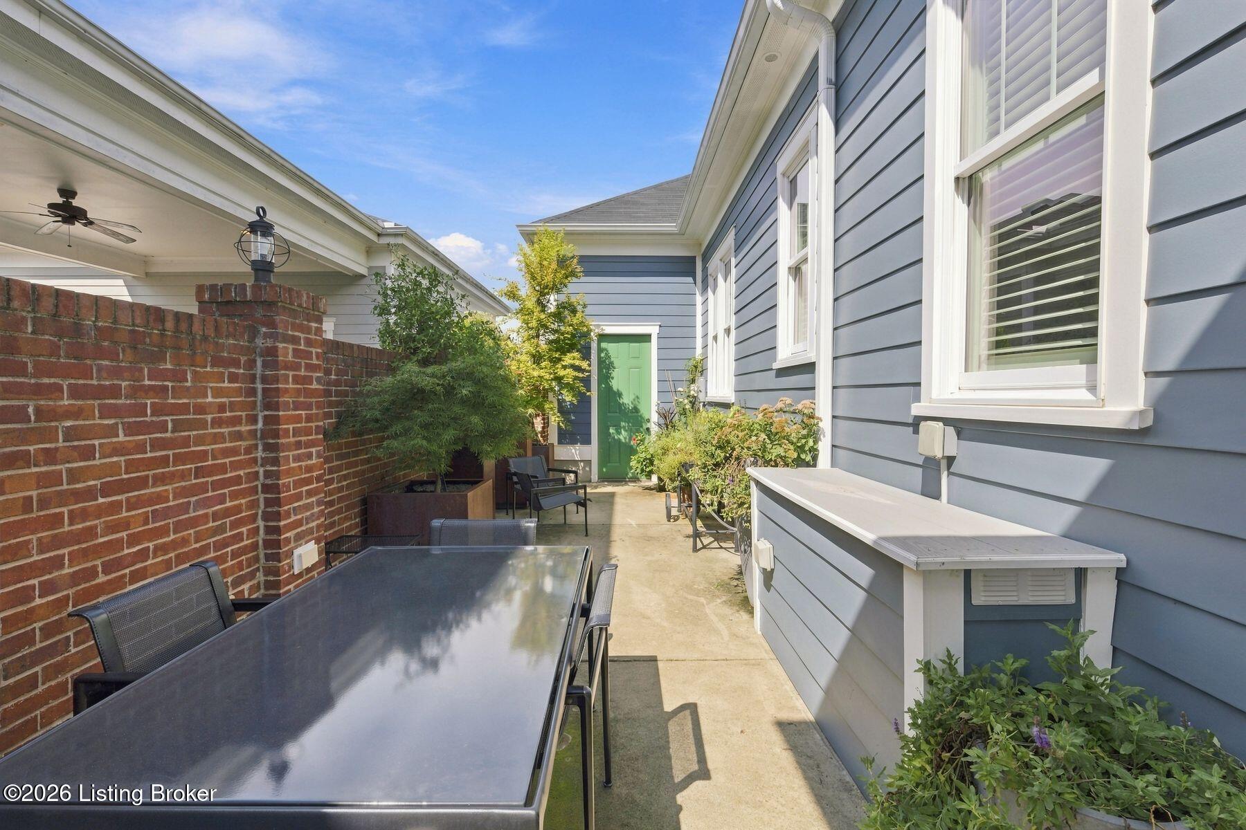 Patio with a dining table, brick privacy wall, potted plants, and a green door.