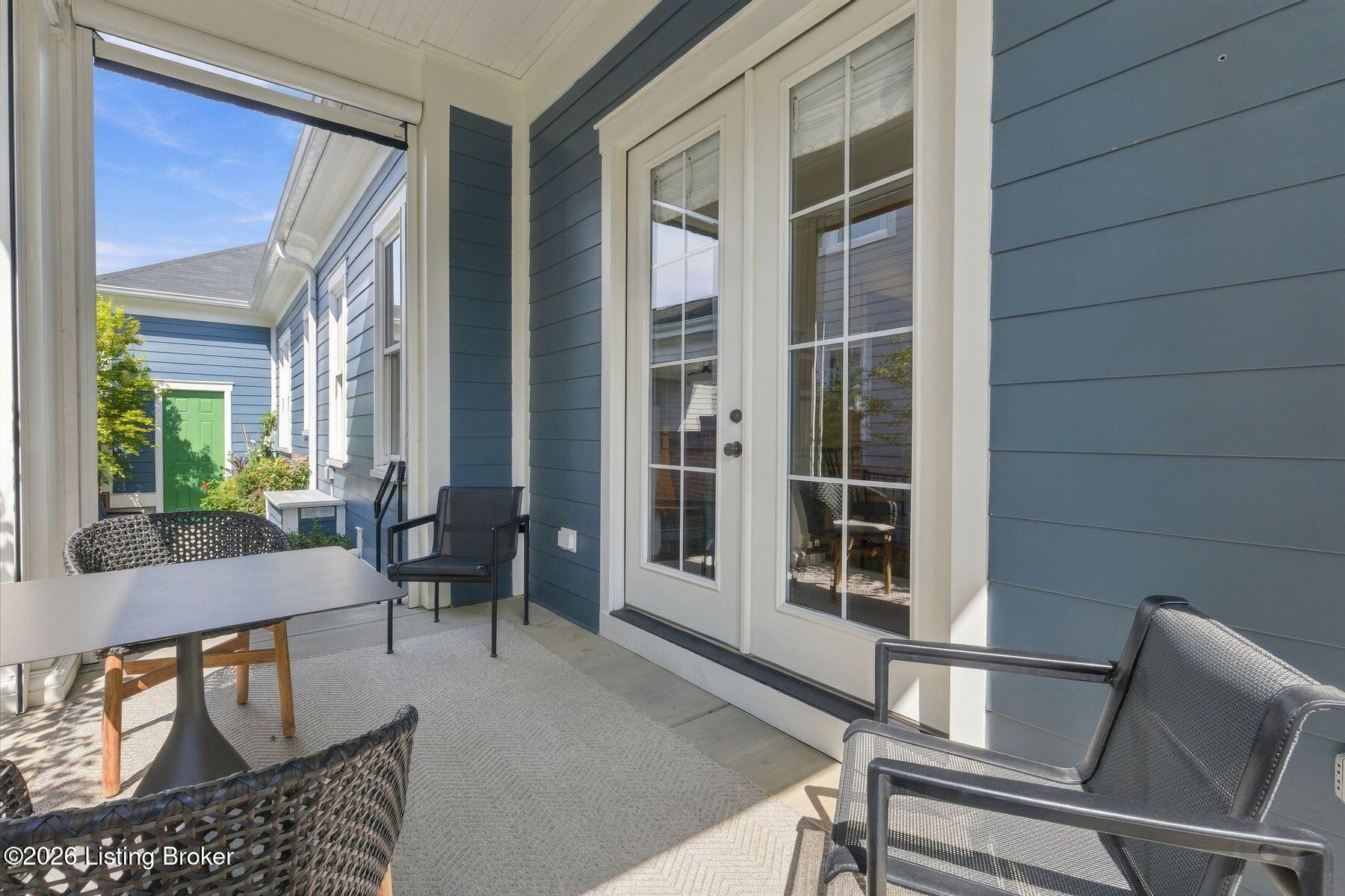 Covered patio with blue siding, glass doors, a dining table, and black woven chairs.