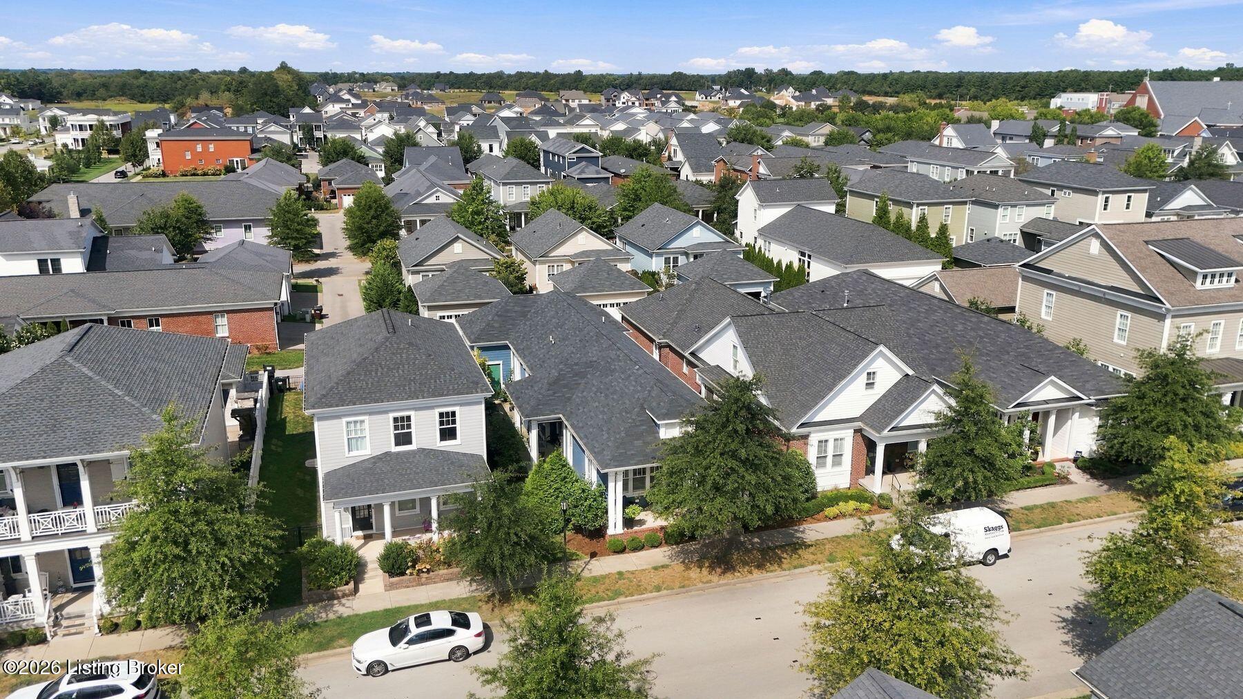 Aerial view of a suburban neighborhood with closely spaced homes, tree-lined streets, and gray roofs.