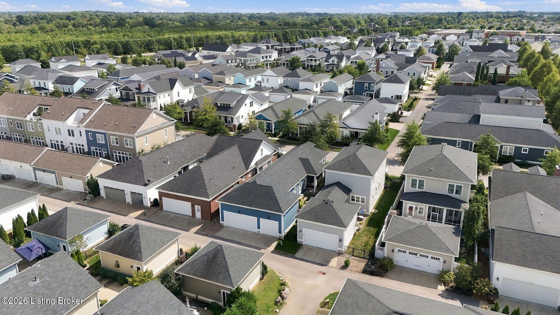 Aerial view of a residential neighborhood with closely spaced homes and woods beyond.