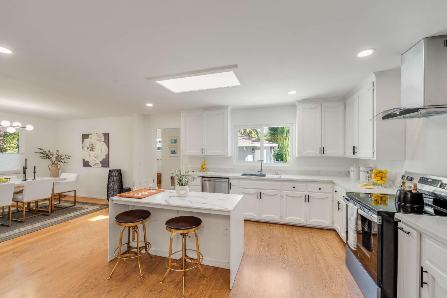 Bright white kitchen with a central island, stainless steel appliances, and adjoining dining area.