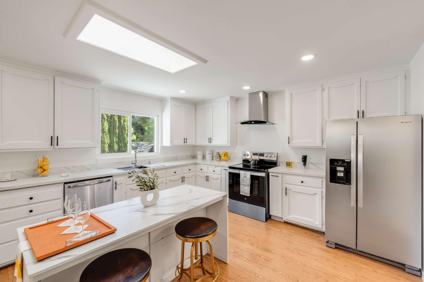 Bright white kitchen with a marble-look island, stainless steel appliances, and warm wood flooring.